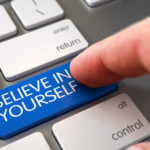 keyboard with white keys and one blue key that says "believe in yourself" and a caucasian finger reaching to press the button