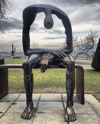 A modern statue depicting a person slumpt over on a bench with their elbows on their knees. 